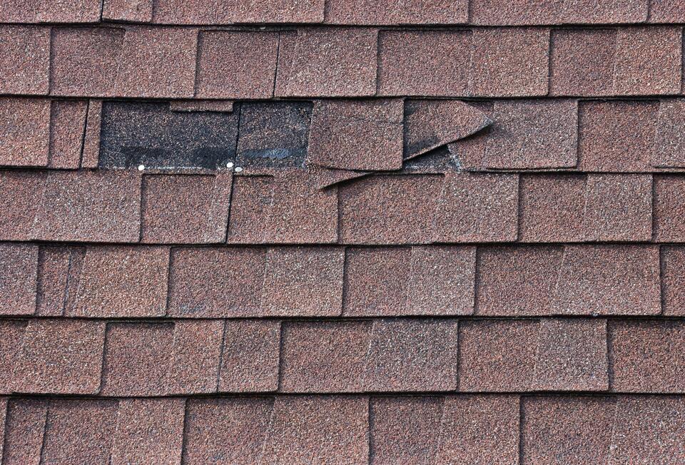 missing shingles-close up of brown architectural shingles on house with missing pieces