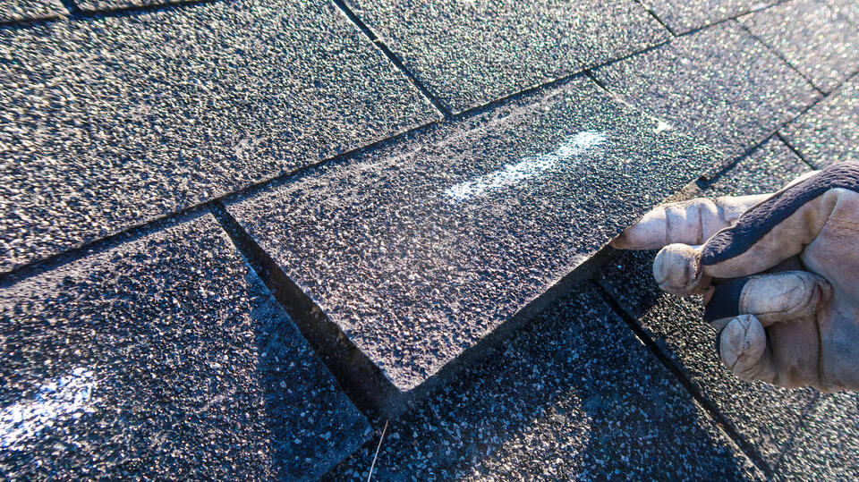 missing shingles-close up of roofer lifting up loose shingle on roof