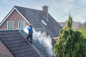 roof washing-roofer standing on ladder power washing roof shingles