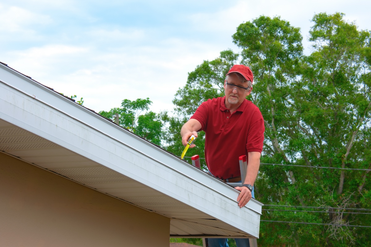 man using measuring tape to inspect roof