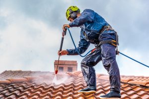 worker using safety rope to power wash tile roof