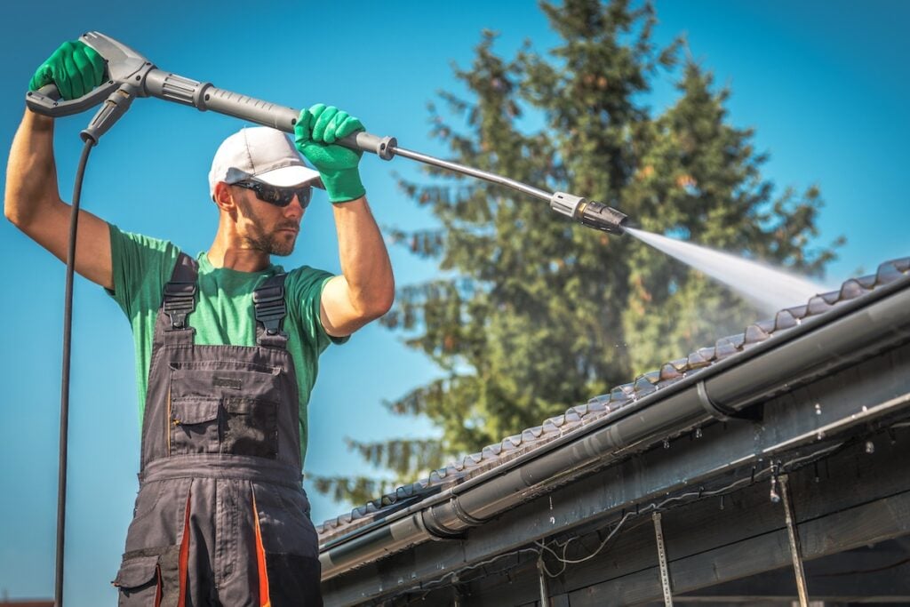 Professional contractor pressure washing a tiled roof and cleaning gutters on a sunny day