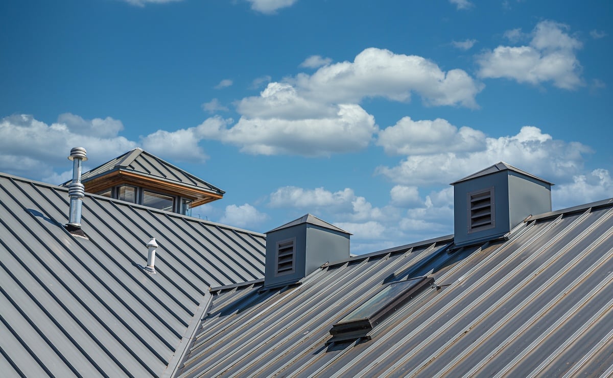 A metal roof with three small cupolas and a vent pipe showcases the quality of metal roofing Franklin TN under a bright blue sky with scattered fluffy white clouds.