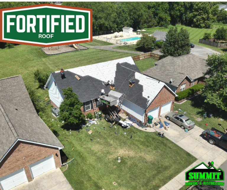 Aerial view of a house with fortified roofers working on a partially completed new roof. Tools and materials are scattered on the lawn. Logo for “FORTIFIED ROOF” is top left, and “SUMMIT Roofing & Restoration” is bottom right.