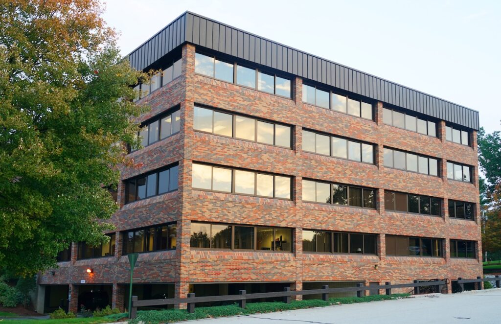 A four-story brick office building with large windows reflecting the sky, surrounded by trees and a paved walkway in front—showcasing quality commercial roofing Clarksville TN businesses can trust.