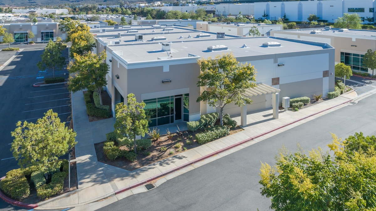 Aerial view of a modern, single-story industrial or office building with a flat roof installed by commercial roofing Waverly TN experts, surrounded by trees, landscaped areas, parking spaces, and nearby similar buildings under a clear sky.