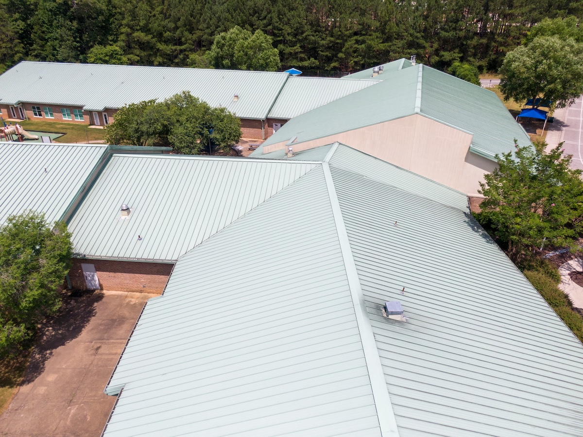 Aerial view of a building complex with green metal roofs surrounded by trees and paved walkways. The commercial roofing in Clarksville, TN, forms striking geometric patterns across the structures.