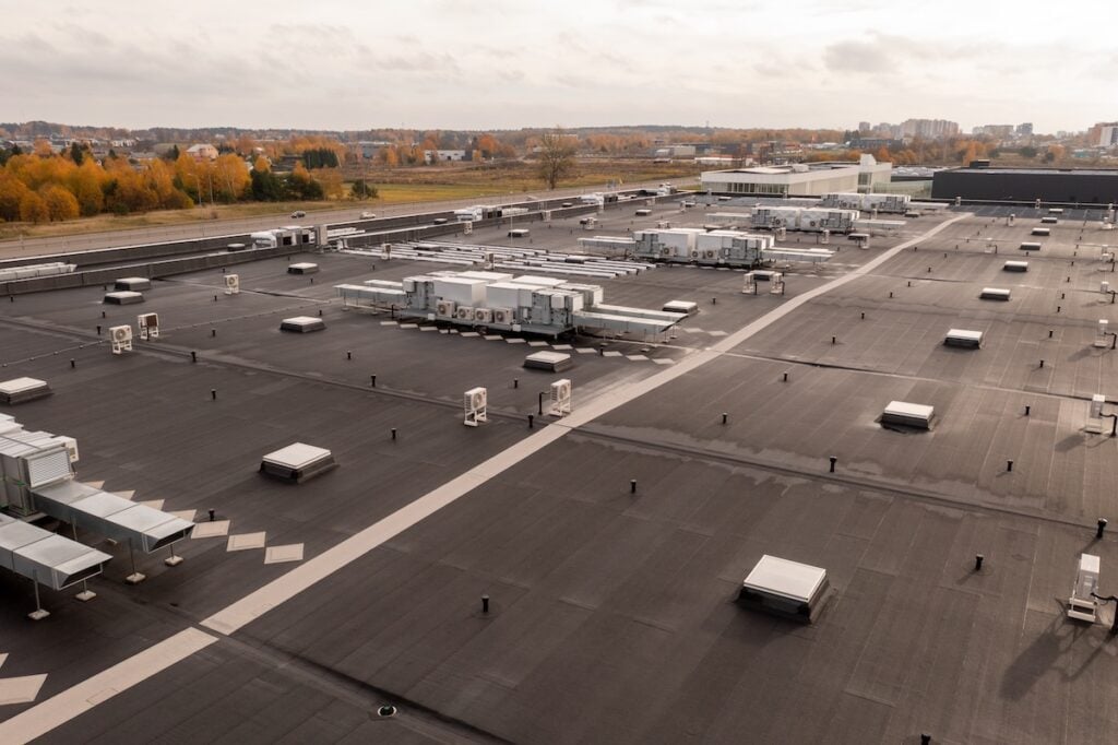 A large flat commercial roofing Milan TN rooftop features multiple HVAC units, vents, and skylights, overlooking a cityscape with autumn trees and buildings in the distance beneath a cloudy sky.