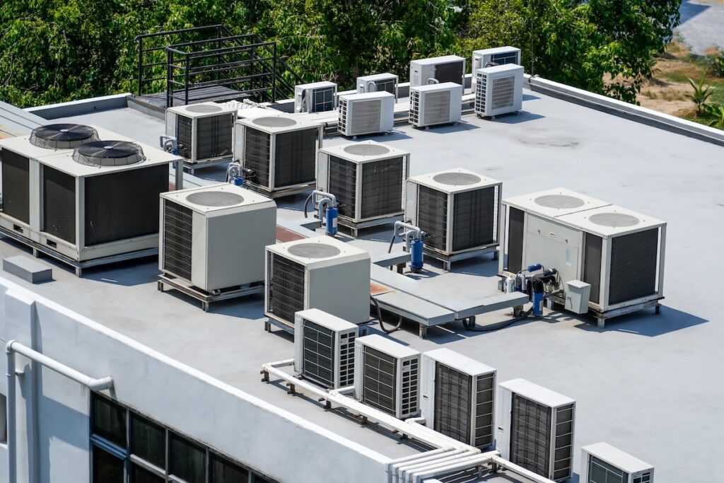 Multiple air conditioning units and ventilation systems are installed on the flat rooftop of a commercial building, showcasing quality commercial roofing Clarksville TN, with trees visible in the background.
