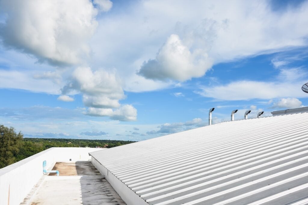 A white metal rooftop, part of a commercial roofing project in Clarksville, TN, stretches under a bright blue sky with scattered clouds. Some trees and greenery are visible in the distance beyond the roof’s edge.