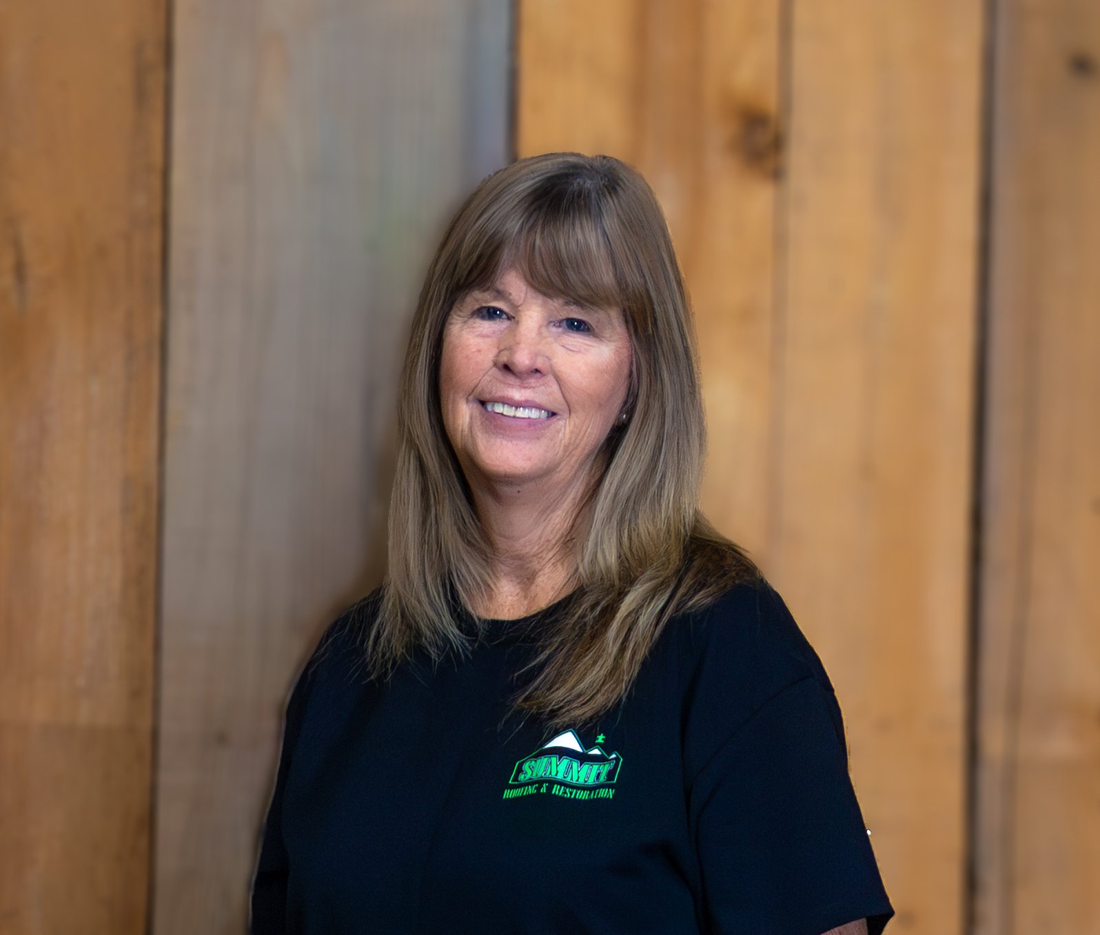 A woman with long light brown hair and bangs, wearing a black t-shirt with a green 