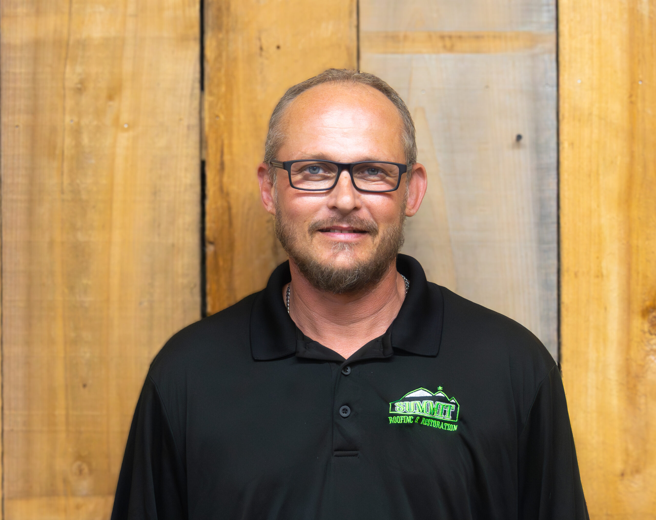 A man with short hair and glasses wearing a black polo shirt with a green