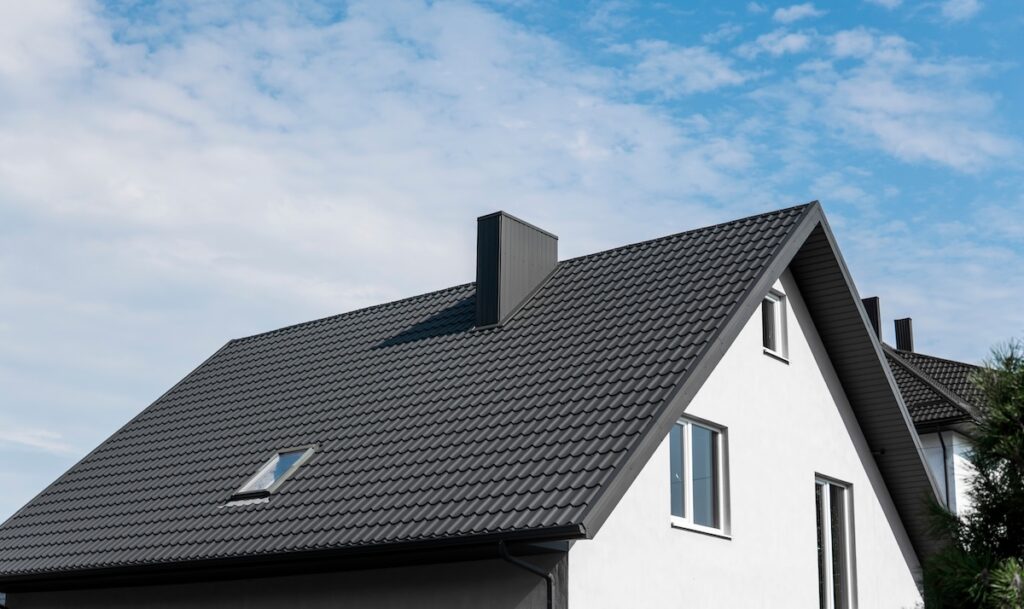 A modern house with a dark tiled roof—one of the most popular roof types—white exterior walls, and several windows, set against a partly cloudy blue sky. roof types
