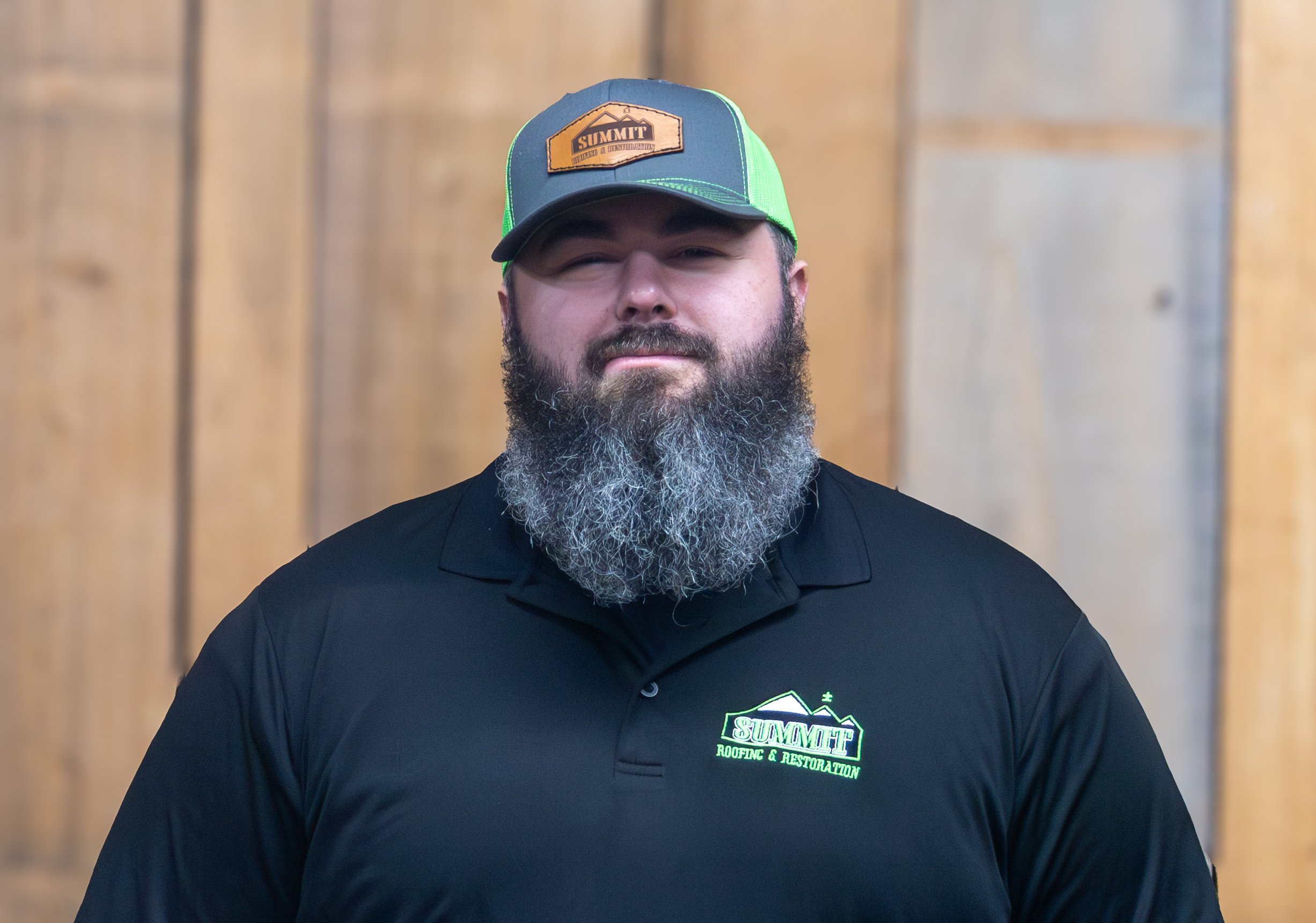 A bearded man in a black polo shirt and green-and-grey cap, both with 